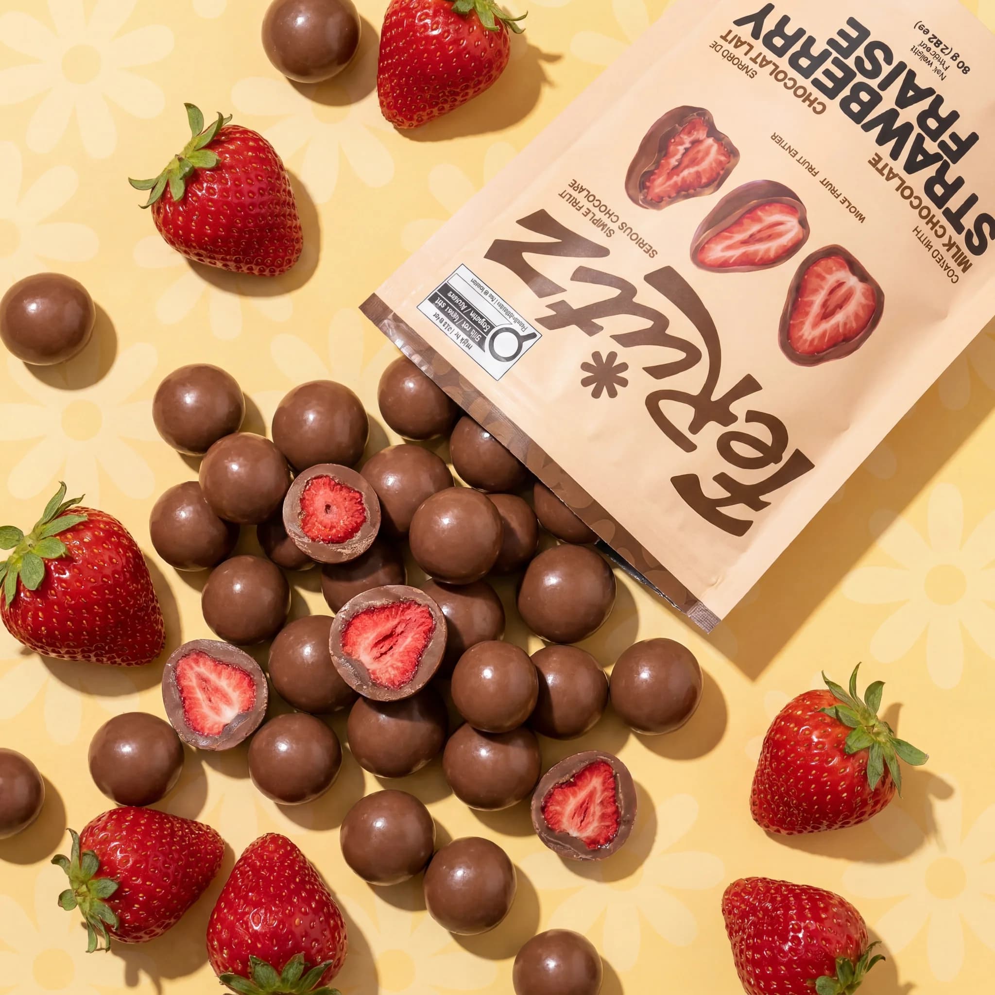 Milk chocolate bites and strawberries scattered over a butter yellow daisy pattern