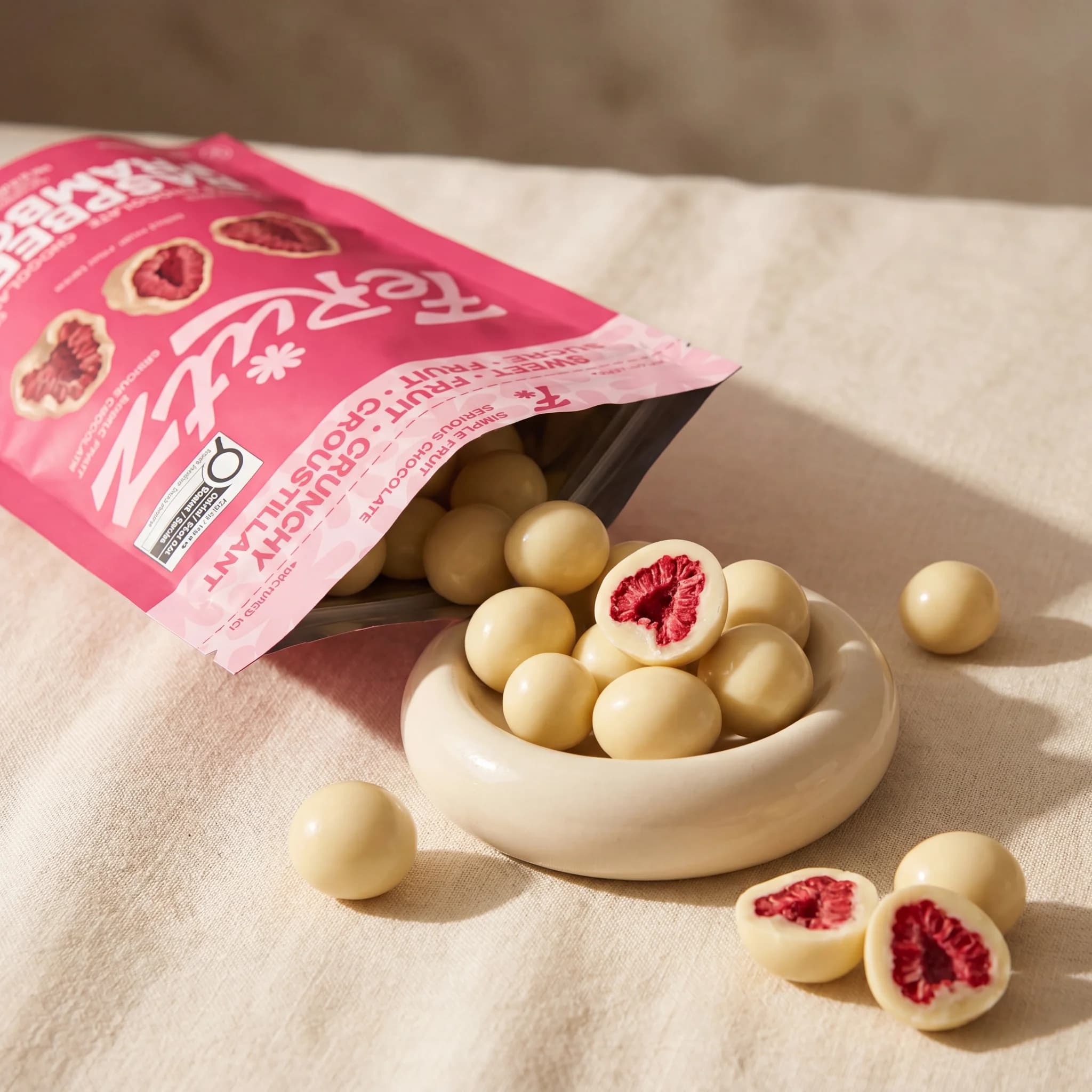 A Ferutz bag pouring white chocolate raspberry bites into a small bowl on linen